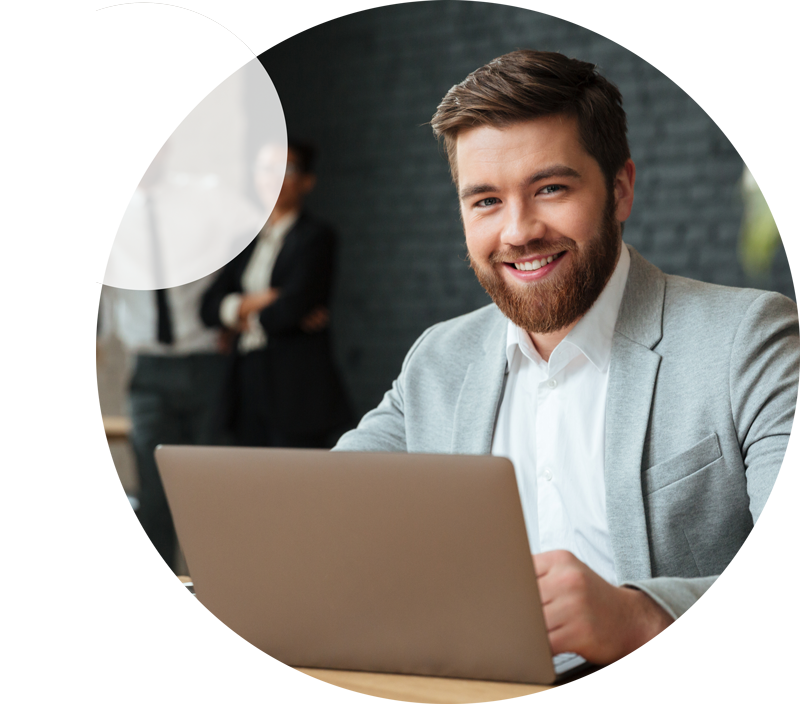 A man smiles at the camera while sitting with a laptop