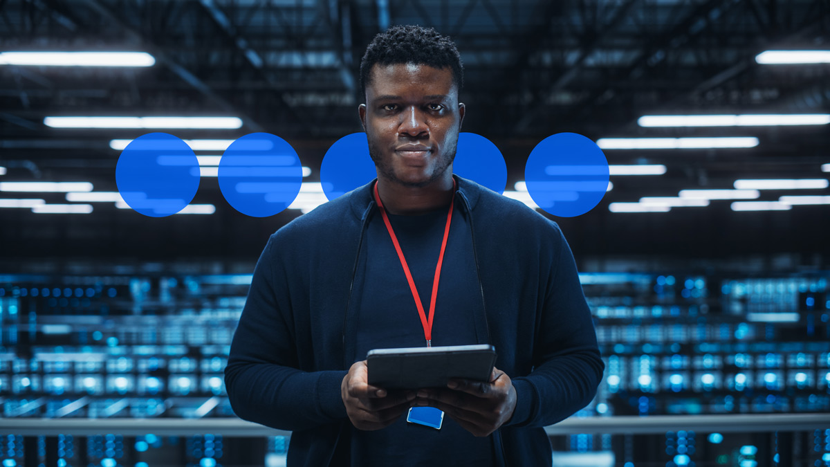 A man with a tablet computer stands in a server room