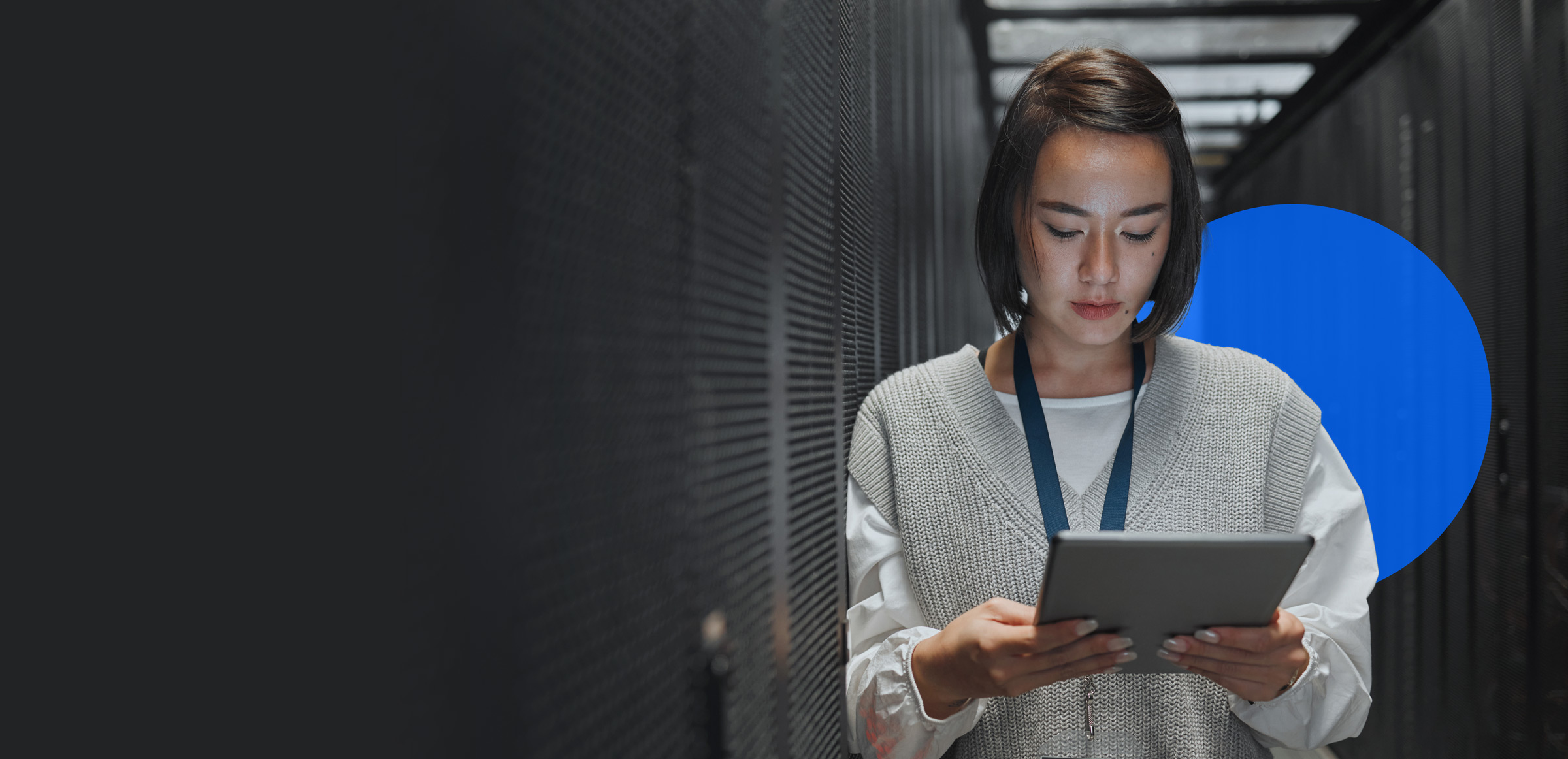 A young woman looks at a tablet computer while leaning against a server rack