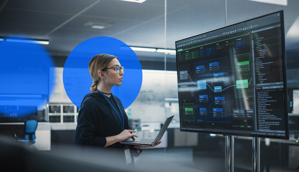 A woman with a laptop looks a large screen