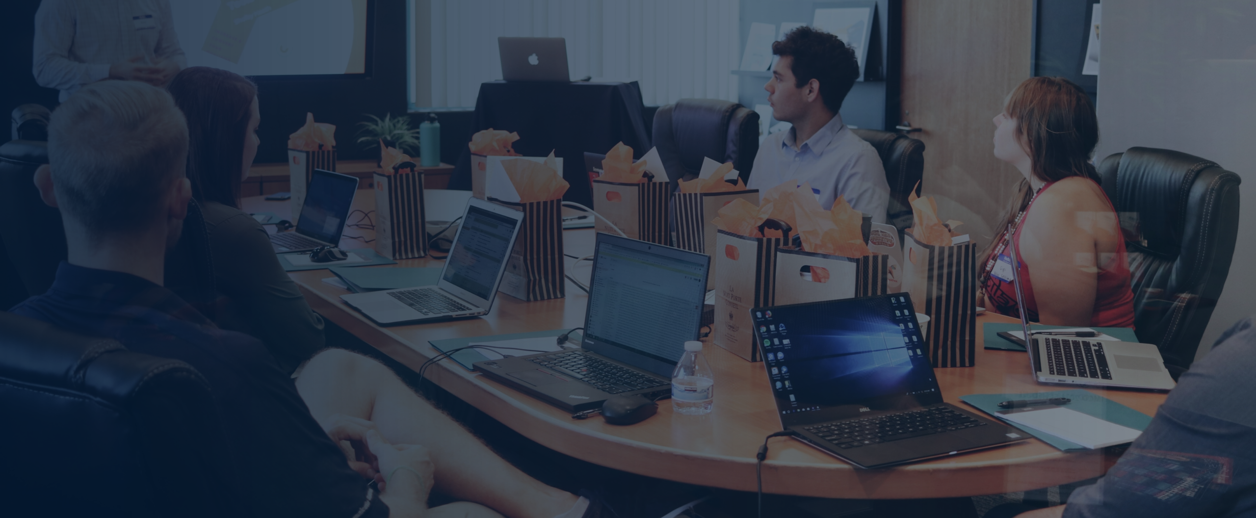 The image shows a team in a meeting with one person presenting