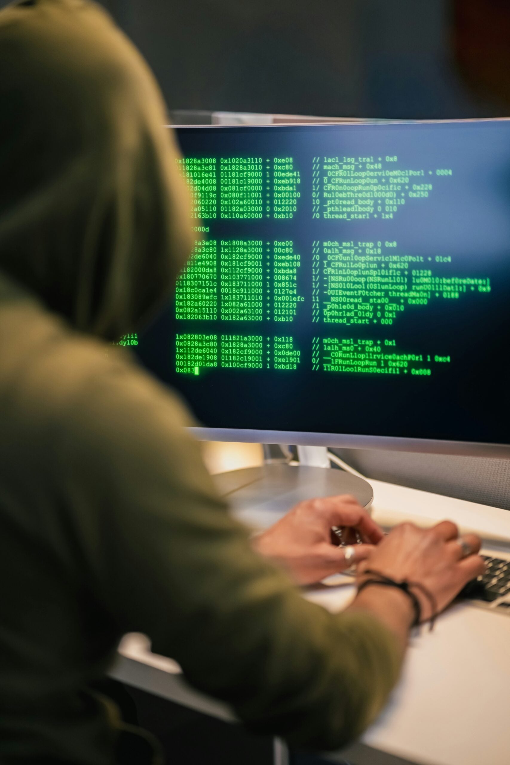 individual in a green hoodie commiting fraud on a computre showing coding