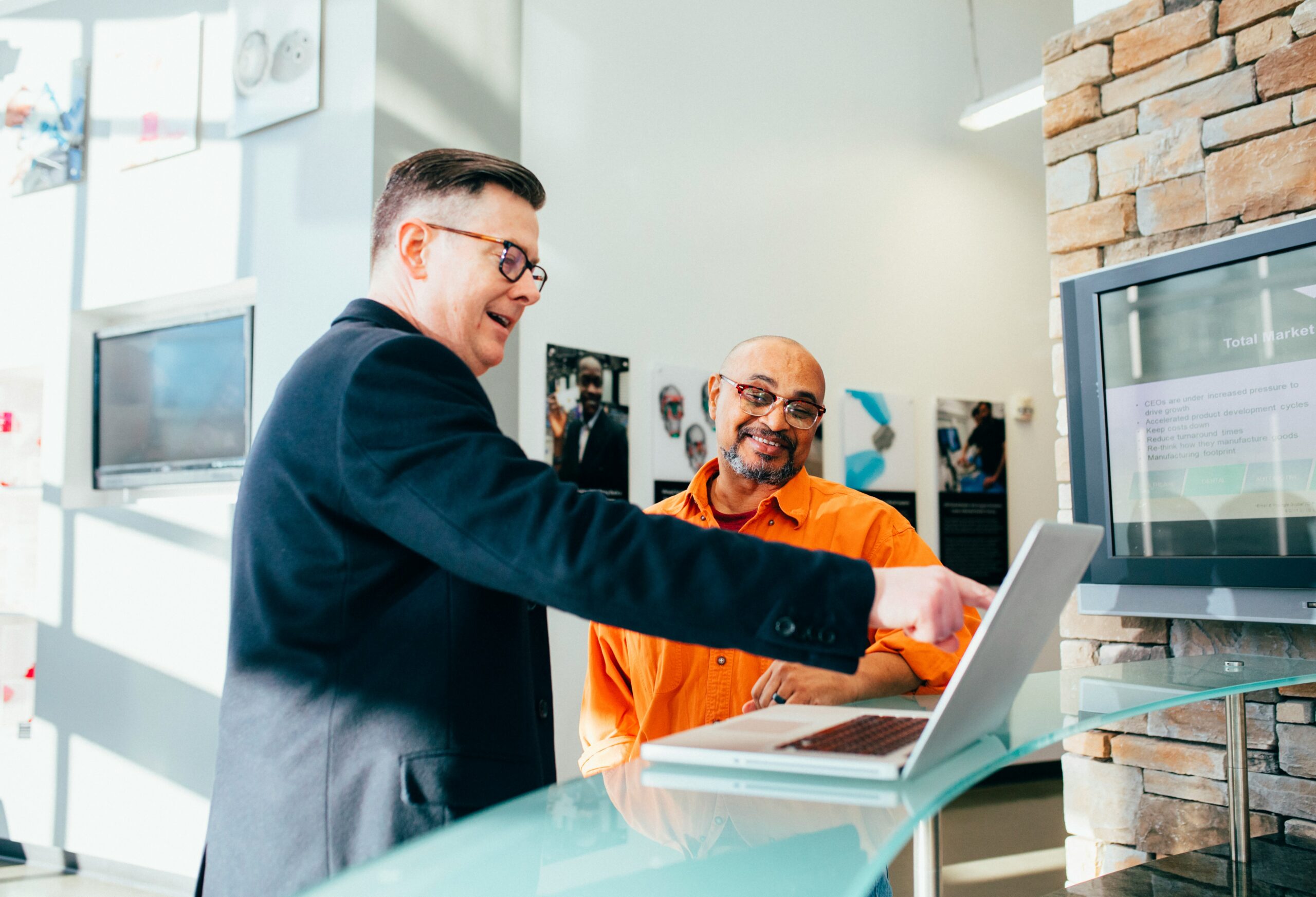 The image shows two men chatting over a laptop